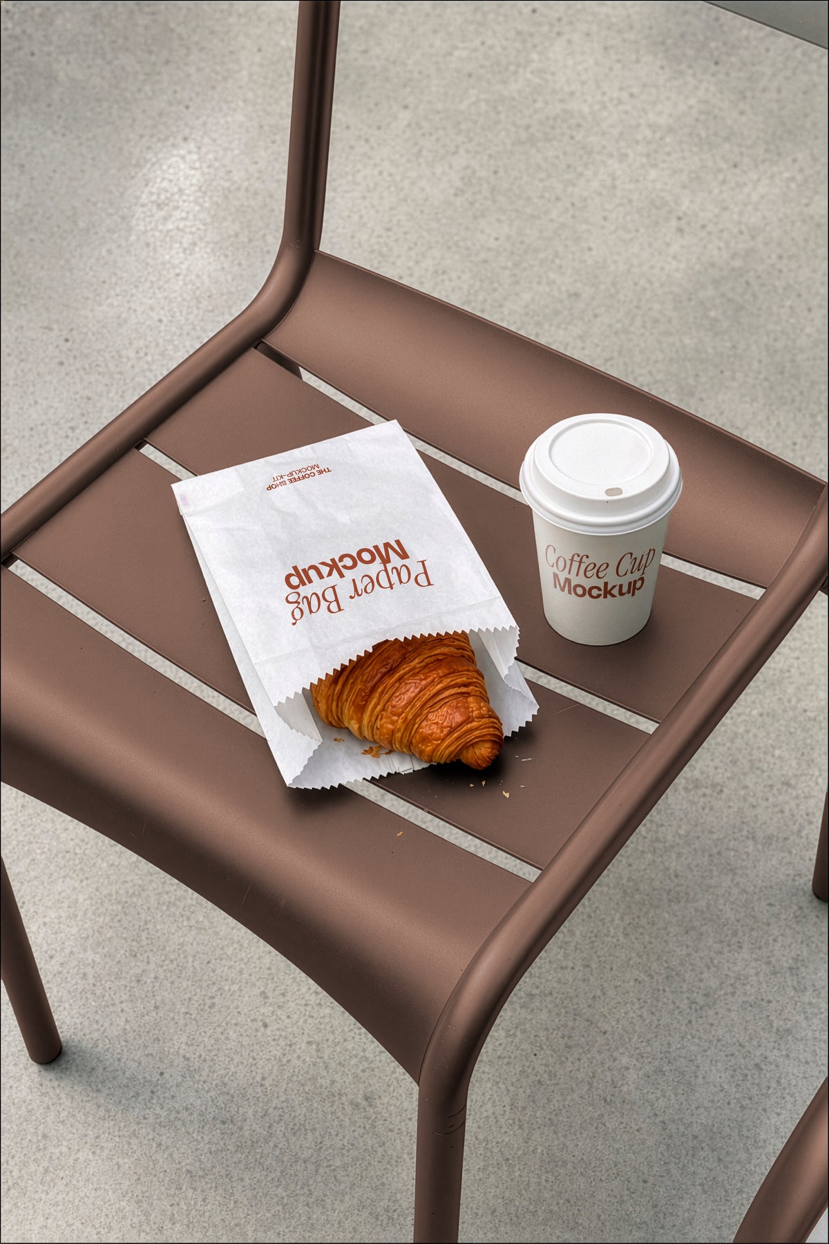 Coffee cup mockup and paper bag mockup styled on a café chair with a croissant. Paper bag mockup and coffee cup mockup together for a coffee shop branding scene. Coffee cup mockup, paper bag mockup, packaging mockup, coffee shop mockup, bakery mockup, café mockup, high quality mockup, PSD file.