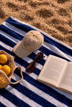Cap mockup PSD on a striped blue and white beach towel with sunglasses, a book, and lemons