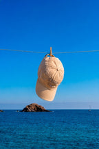Cap mockup PSD hanging from a clothesline over the ocean with a clear blue sky and distant sailboat