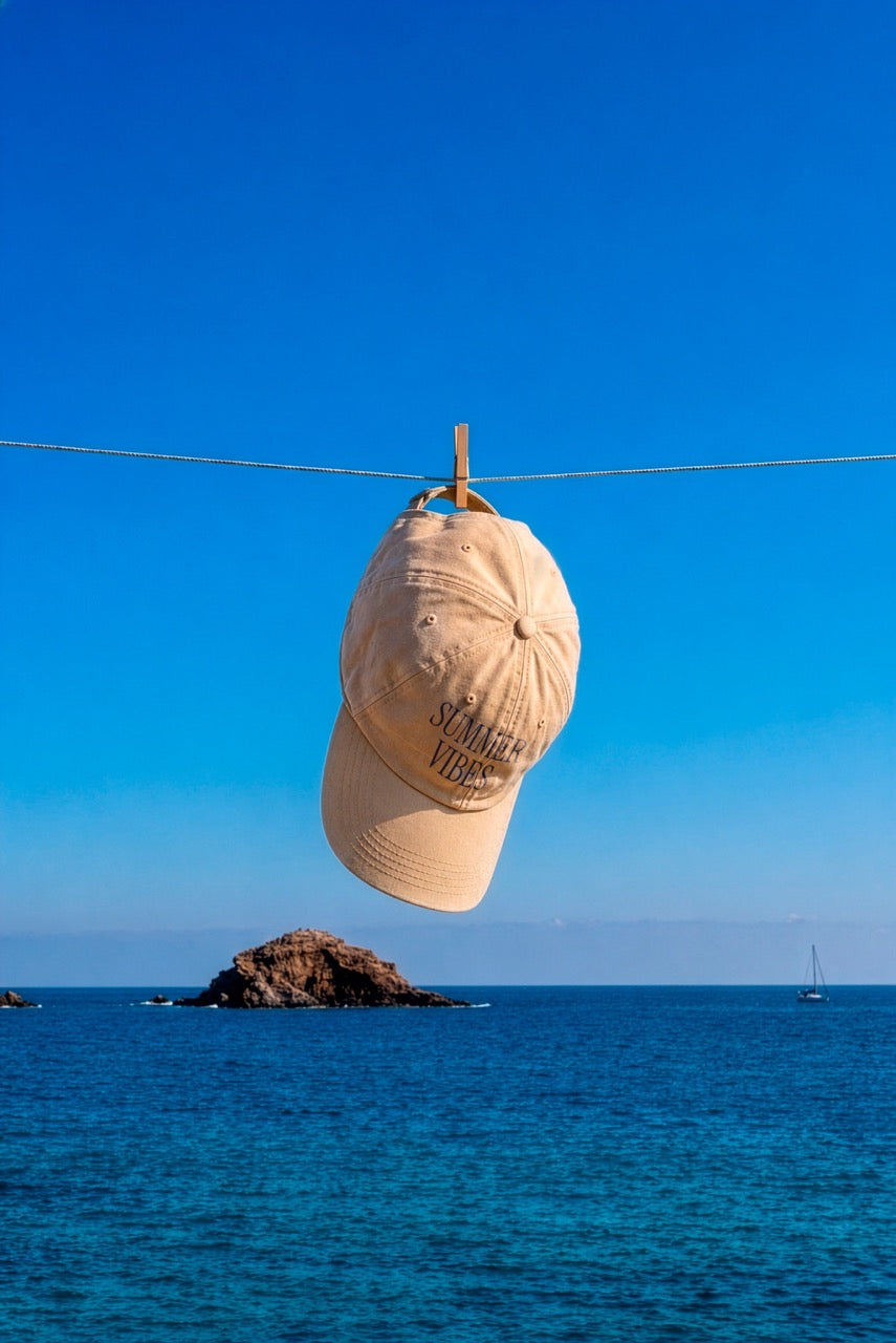 Cap mockup PSD hanging from a clothesline over the ocean with a clear blue sky and distant sailboat