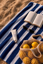 Hand cream tube mockup PSD on a striped beach towel with sunglasses, a book, and lemons