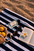 Perfume bottle mockup PSD on a striped beach towel with sunglasses, a frangipani flower, and lemons