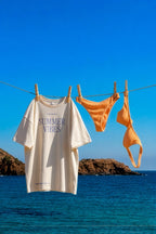 Oversized t-shirt and orange bikini set mockup PSD hanging on a clothesline by the sea