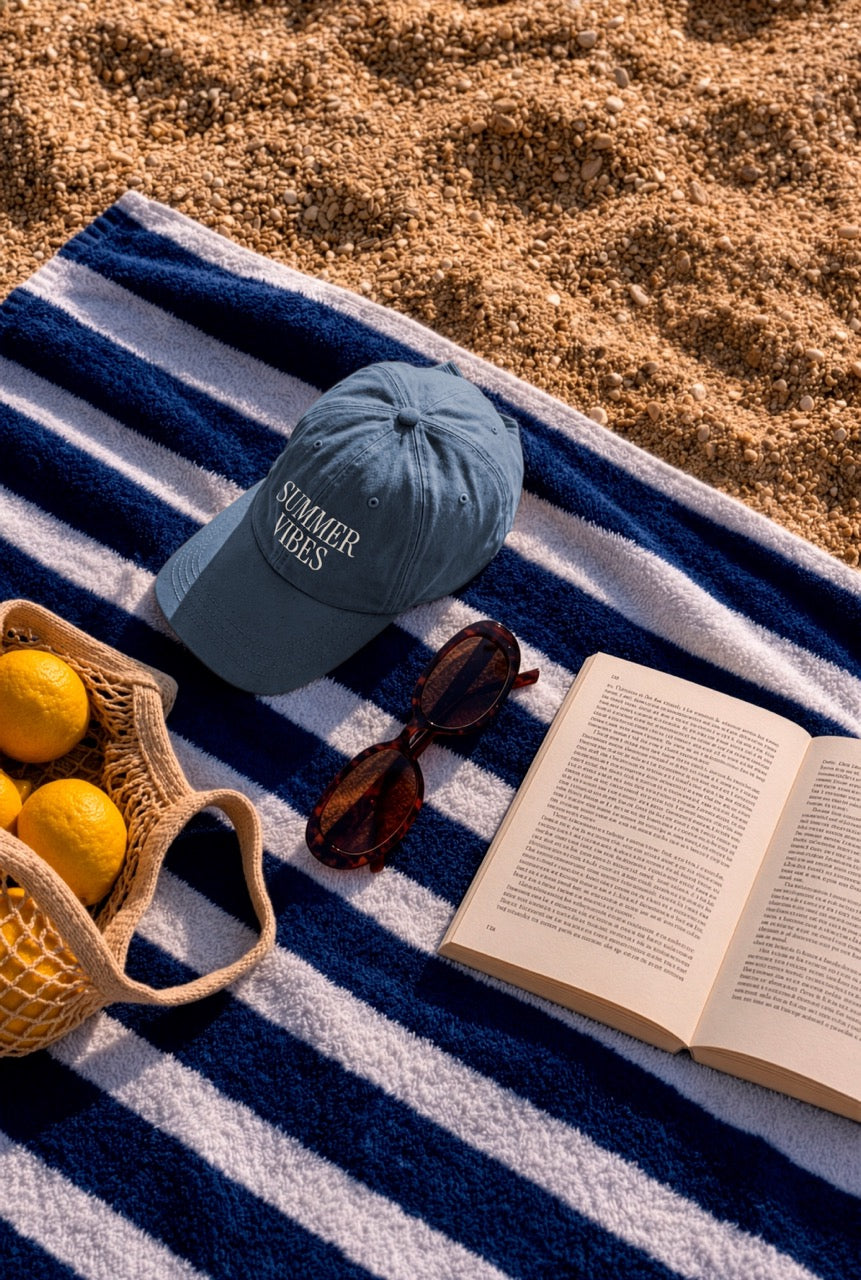Cap mockup PSD on a striped blue and white beach towel with sunglasses, a book, and lemons