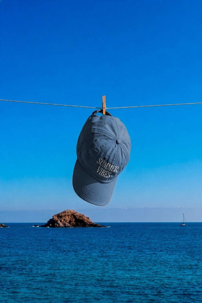 Cap mockup PSD hanging from a clothesline over the ocean with a clear blue sky and distant sailboat