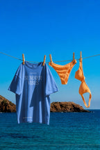 Oversized t-shirt and orange bikini set mockup PSD hanging on a clothesline by the sea