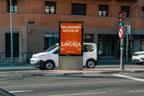Real photo citylight street billboard mockup PSD at intersection with natural light and passing cars