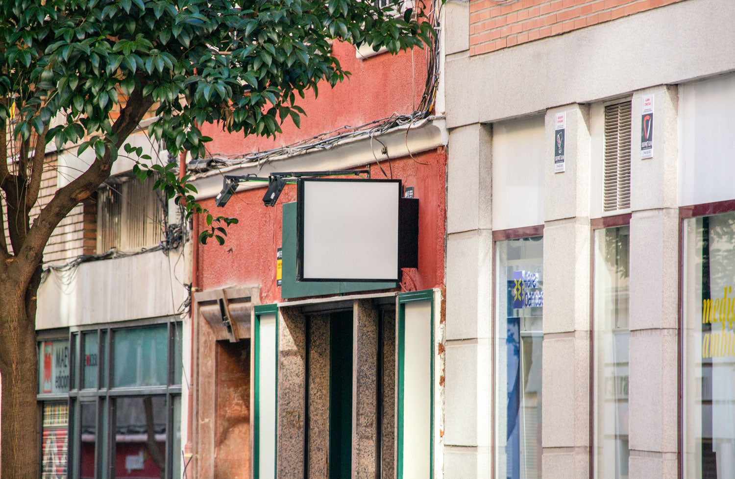 Real photo storefront square logo sign mockup on city street with natural light and shadows
