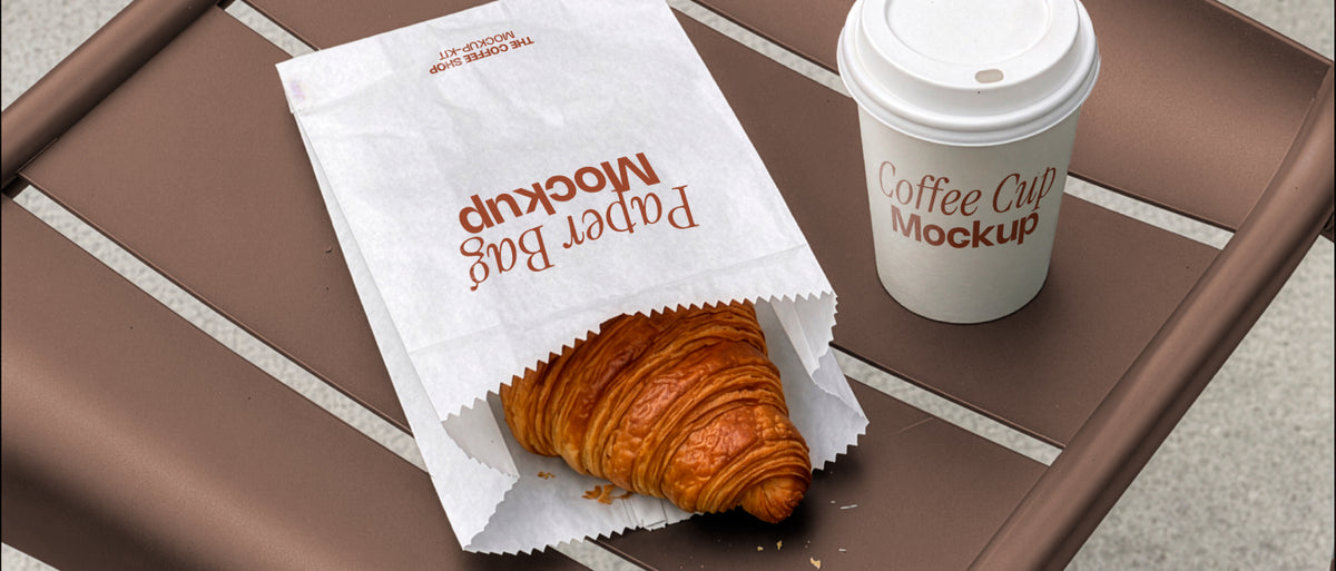 Coffee cup mockup and paper bag mockup styled on a café chair with a croissant. Paper bag mockup and coffee cup mockup together for a coffee shop branding scene. Coffee cup mockup, paper bag mockup, packaging mockup, coffee shop mockup, bakery mockup, café mockup, high quality mockup, PSD file.