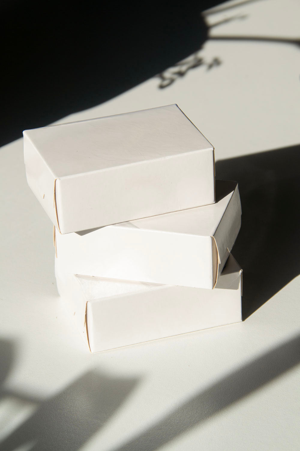 box packaging mockup PSD with three stacked paper boxes on sunlit desk and plant shadows