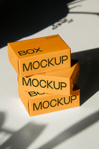 box packaging mockup PSD with three stacked paper boxes on sunlit desk and plant shadows