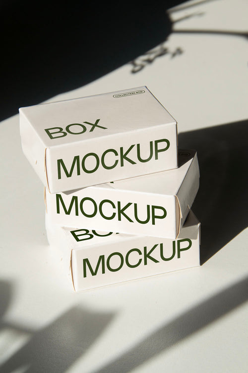 box packaging mockup PSD with three stacked paper boxes on sunlit desk and plant shadows