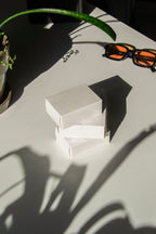 box packaging mockup PSD with three stacked paper boxes on sunlit desk and plant shadows