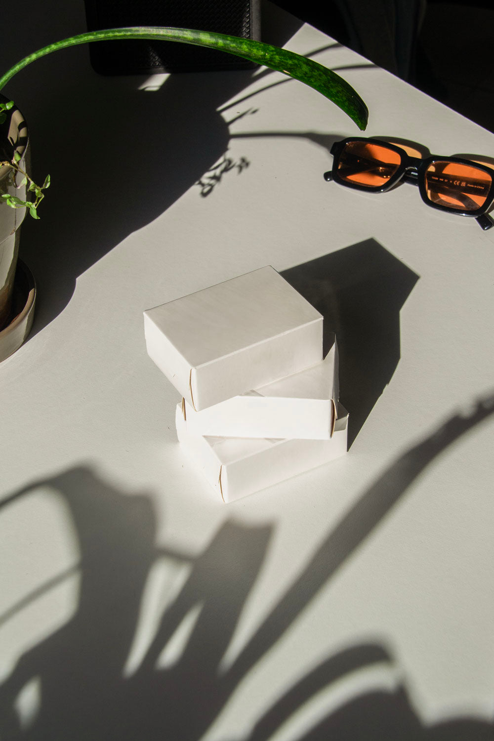 box packaging mockup PSD with three stacked paper boxes on sunlit desk and plant shadows