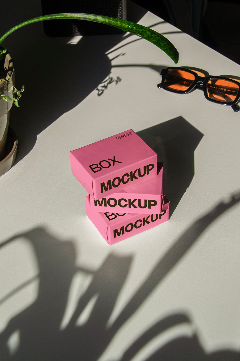 box packaging mockup PSD with three stacked paper boxes on sunlit desk and plant shadows