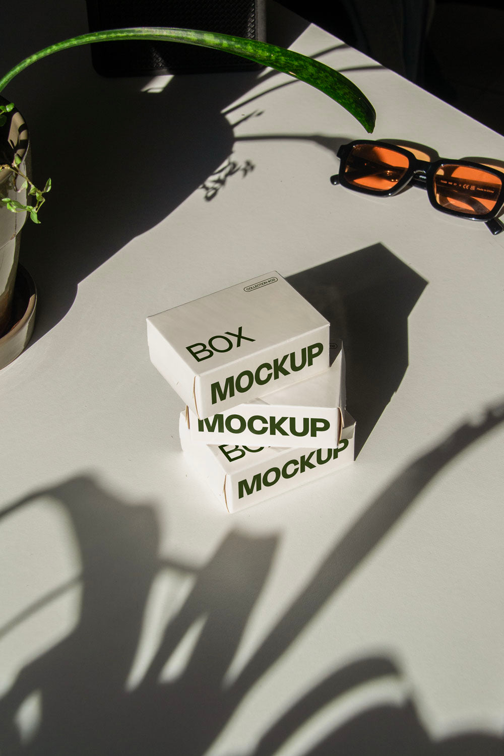 box packaging mockup PSD with three stacked paper boxes on sunlit desk and plant shadows