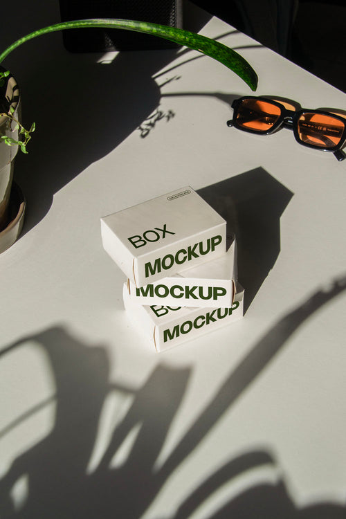 box packaging mockup PSD with three stacked paper boxes on sunlit desk and plant shadows
