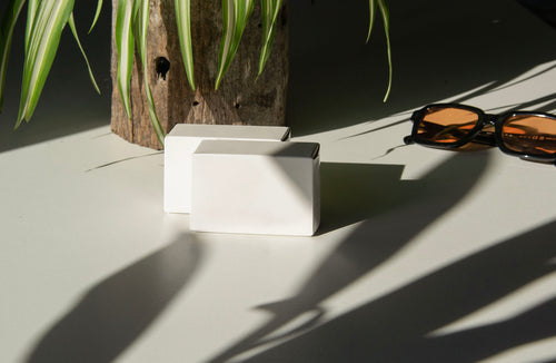 box packaging mockup PSD with three stacked paper boxes on sunlit desk and plant shadows
