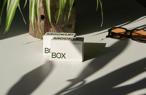 box packaging mockup PSD with three stacked paper boxes on sunlit desk and plant shadows
