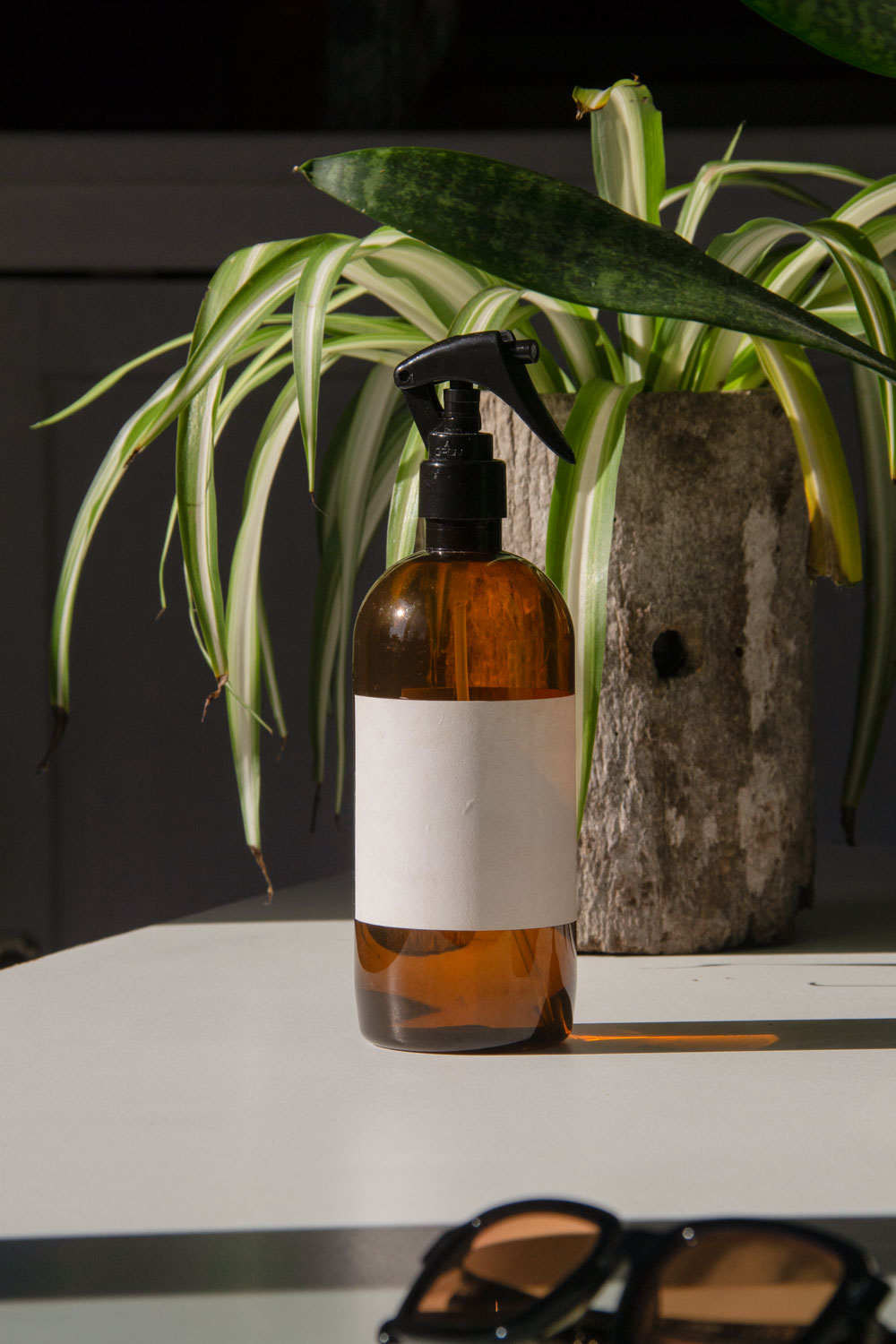 fabric spray bottle label mockup PSD on sunlit table with plant shadows and amber glass