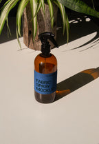 fabric spray bottle label mockup PSD on sunlit table with plant shadows and amber glass