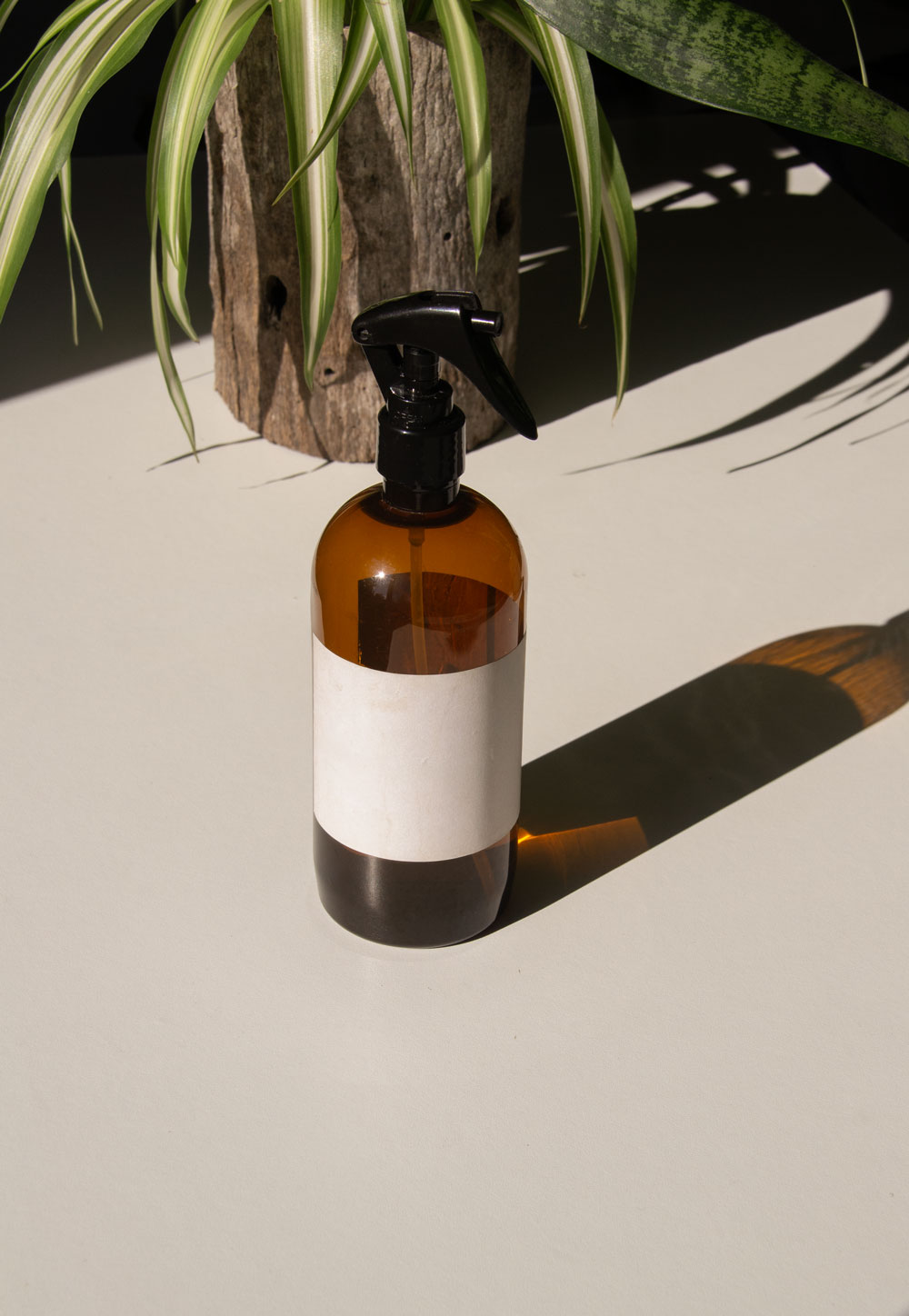 fabric spray bottle label mockup PSD on sunlit table with plant shadows and amber glass