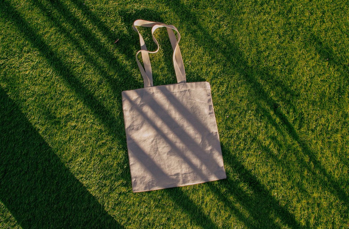 tote bag mockup PSD on sunlit grass with natural shadows and visible fabric texture