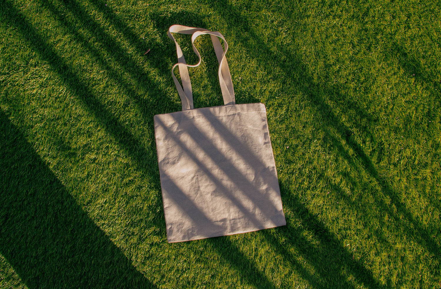 tote bag mockup PSD on sunlit grass with natural shadows and visible fabric texture