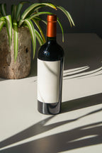 wine bottle label mockup PSD on sunlit table with plant shadows and glass reflections
