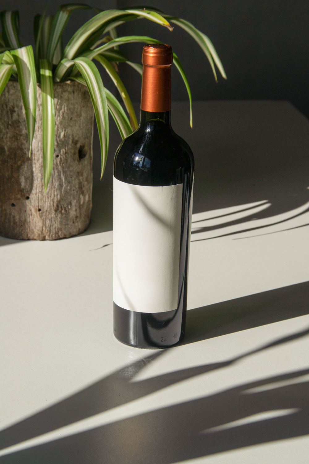 wine bottle label mockup PSD on sunlit table with plant shadows and glass reflections
