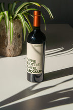 wine bottle label mockup PSD on sunlit table with plant shadows and glass reflections
