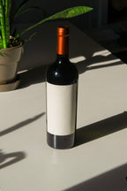 wine bottle label mockup PSD on sunlit table with plant shadows and glass reflections
