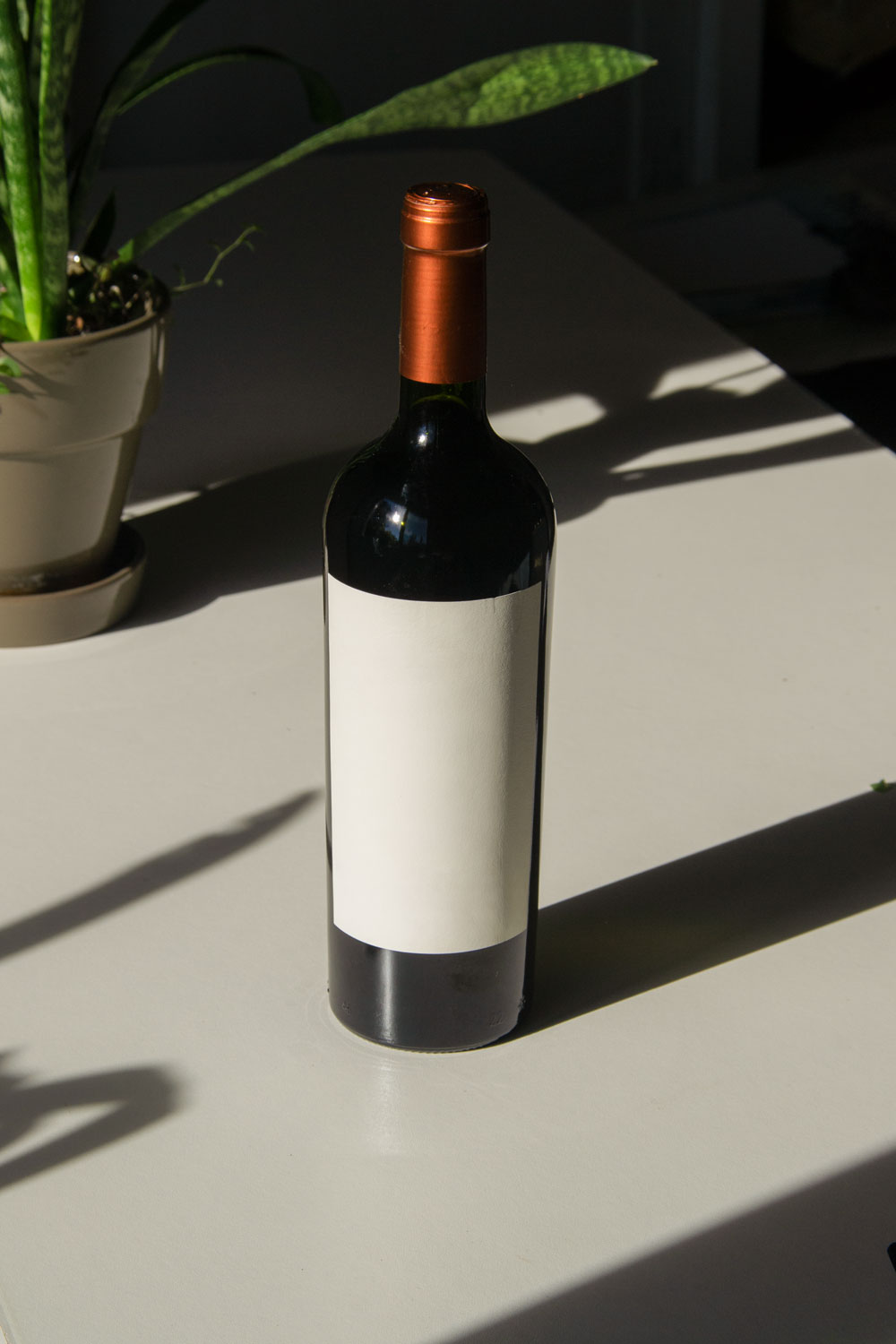 wine bottle label mockup PSD on sunlit table with plant shadows and glass reflections
