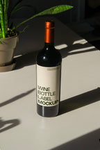 wine bottle label mockup PSD on sunlit table with plant shadows and glass reflections
