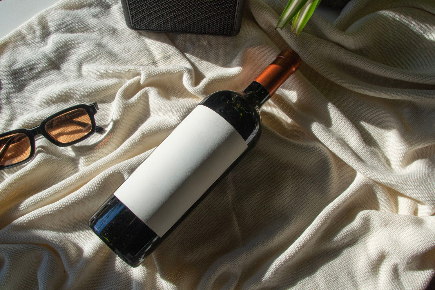 wine bottle label mockup PSD on sunlit table with plant shadows and glass reflections
