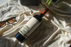 wine bottle label mockup PSD on sunlit table with plant shadows and glass reflections
