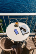 iPhone mockup PSD on a balcony table overlooking the ocean with coffee and sunglasses