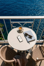 iPhone mockup PSD on a balcony table overlooking the ocean with coffee and sunglasses